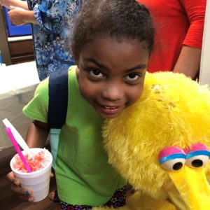 child poses with a snowcone and Big Bird